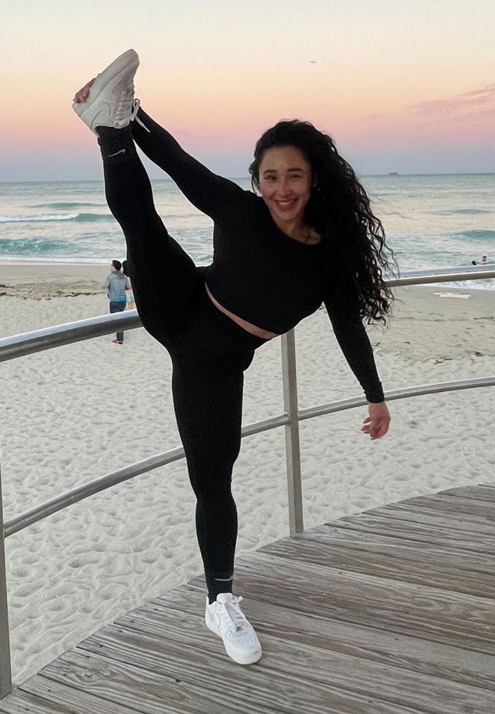 Coach in black outfit in the beach is streching and holding her leg.